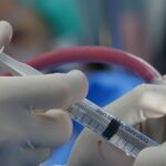 Surgeon's hands handling syringe during a medical procedure in a sterile operating room.