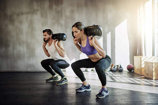 Shot of two young people working out in the gym using weighted bags