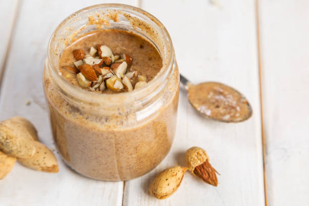 Almond butter in glass jar, white wood background