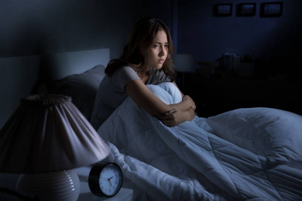 Depressed young Asian woman sitting in bed cannot sleep from insomnia