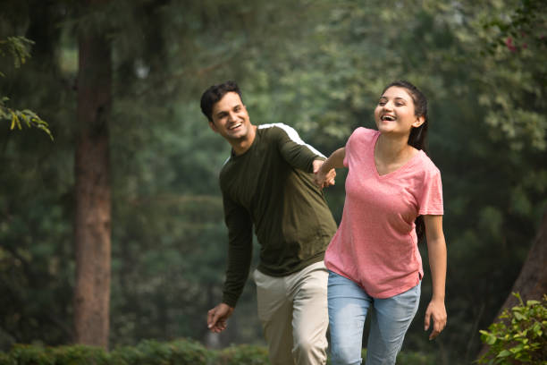Woman holding hands and pulling front her carefree boyfriend having fun at park