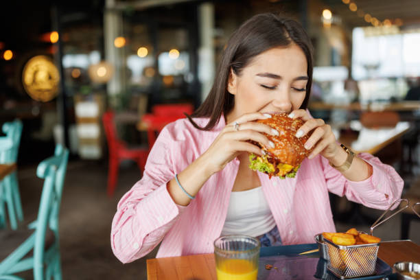 Young woman eating cheeseburger and French fries in fast food restaurant