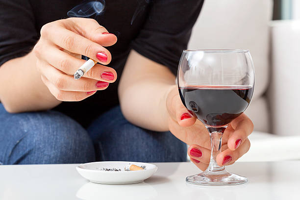 Young woman addicted to cigarettes and alcohol sitting by the table at home