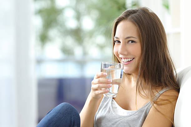 Girl drinking water sitting on a couch at home and looking at camera
