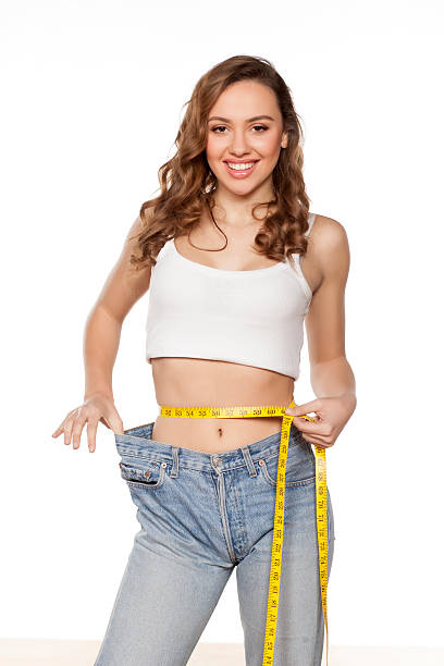 happy young woman posing with a measuring tape and a big size pants