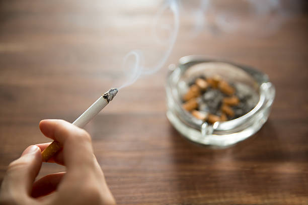 Young woman holding burning cigarette in hand with ashtray