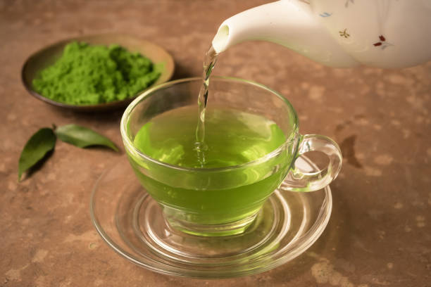 Green tea being poured into glass tea cup on the table
