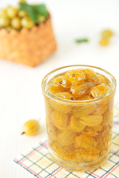 Glass with yellow gooseberry jam on table